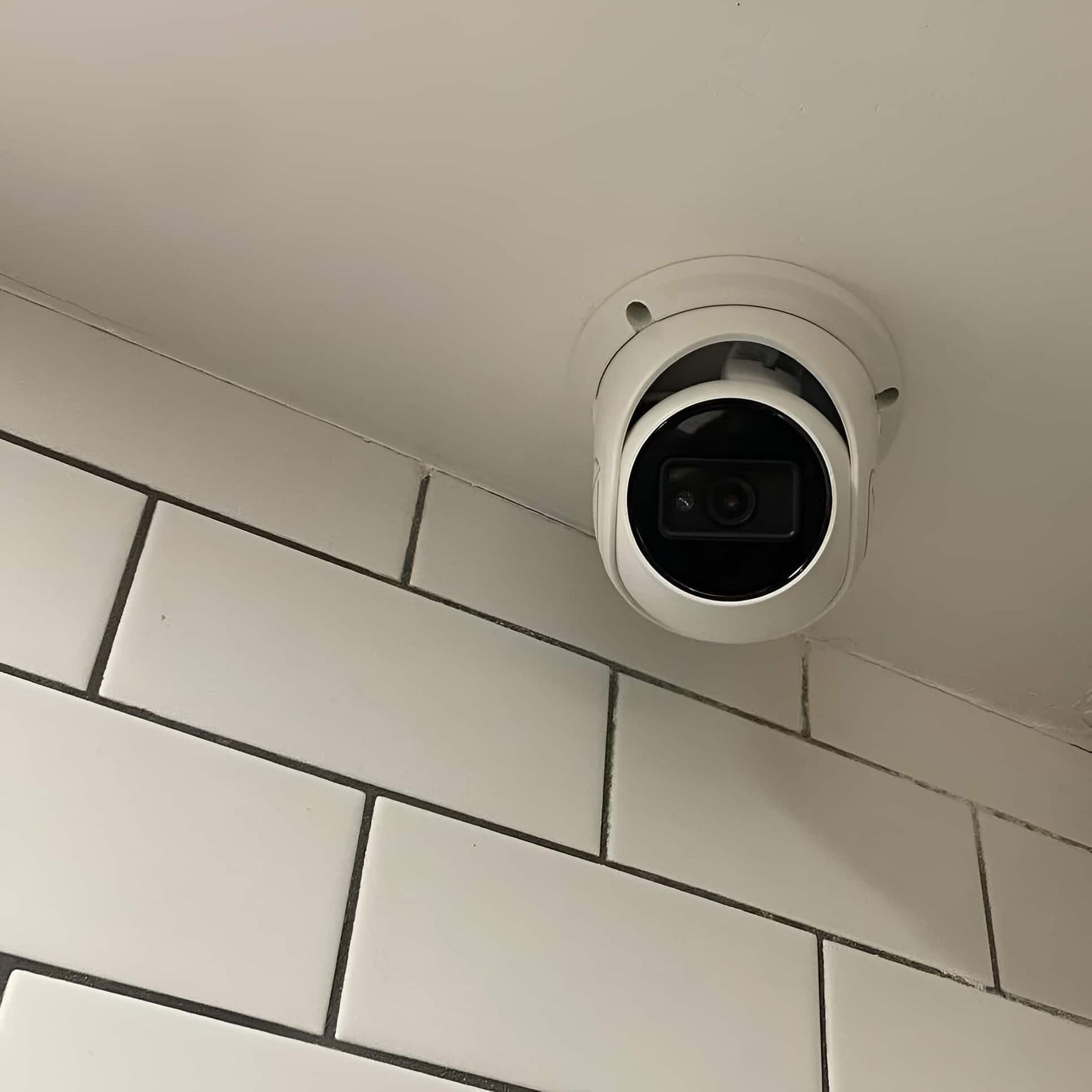 White Security Camera Mounted on a White Ceiling Next to White Tiled Wall — SparkSafe Electrical in Dapto, NSW