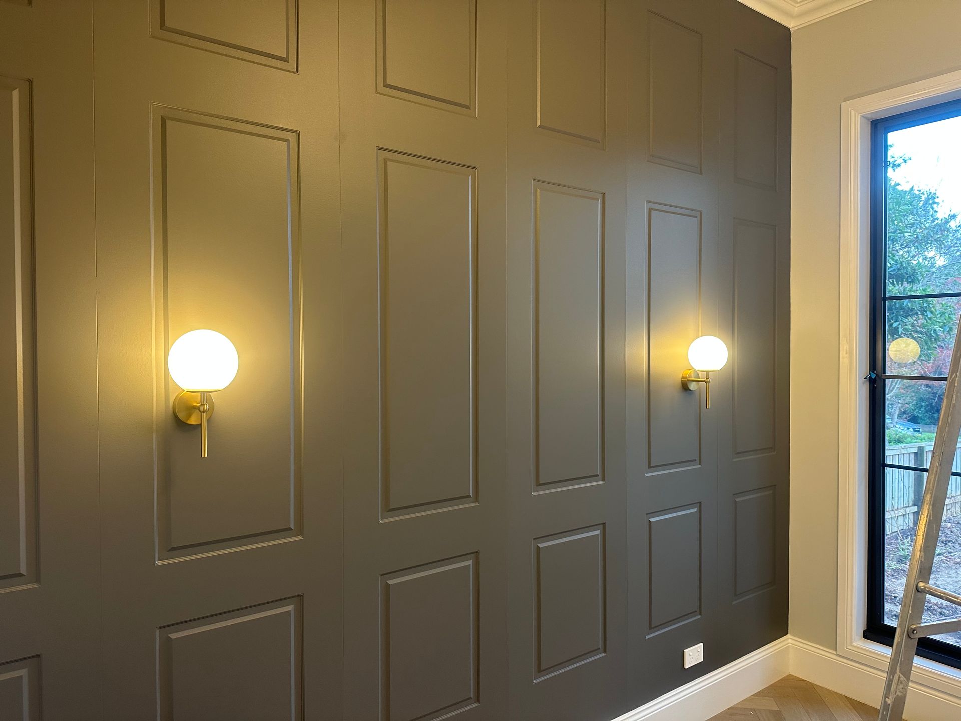 Gray paneled wall with two globe lights, a window, and a ladder — SparkSafe Electrical in Gerringong, NSW