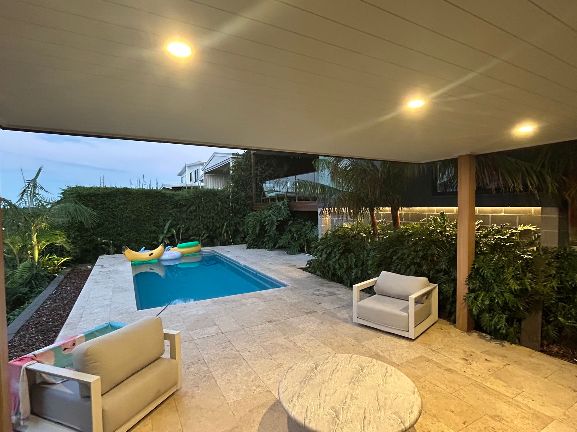 Outdoor patio with a pool, two chairs, and lush greenery — SparkSafe Electrical in Kiama, NSW