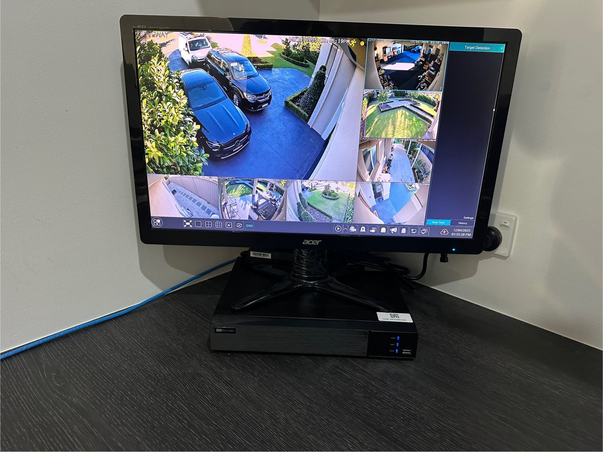 Security camera monitor displaying multiple views of a driveway and yard. Monitor and DVR on a corner desk  — SparkSafe Electrical in Dapto, NSW