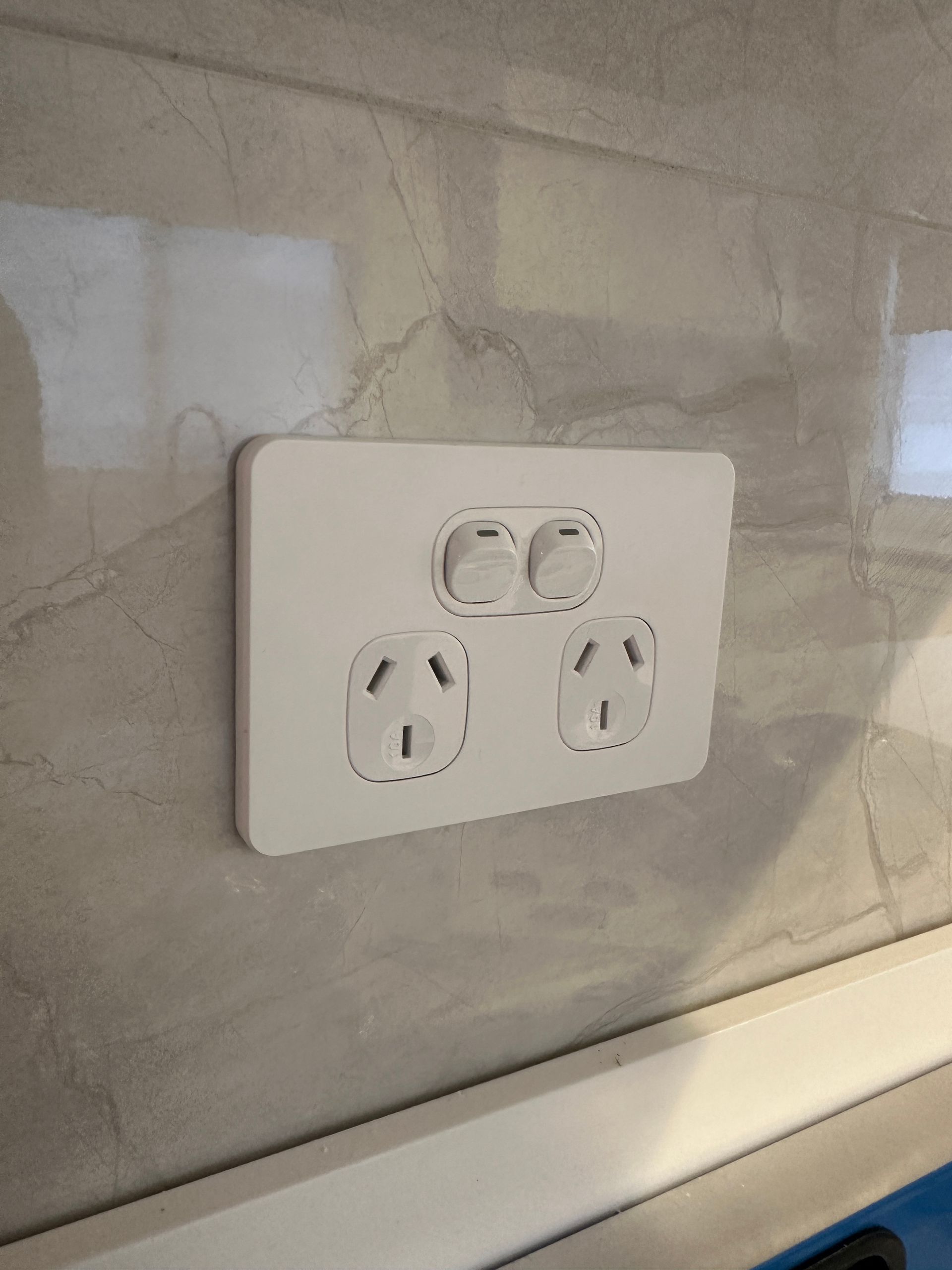 White electrical outlet with two switches on a marble-tiled wall  — SparkSafe Electrical in Dapto, NSW