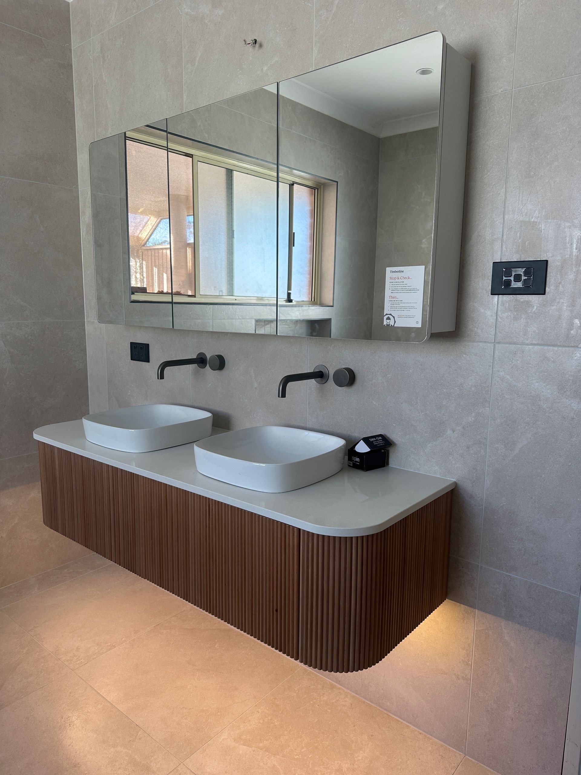 Modern bathroom with double sinks and a large mirror. Brown wood vanity with white sinks, grey walls  — SparkSafe Electrical in Dapto, NSW