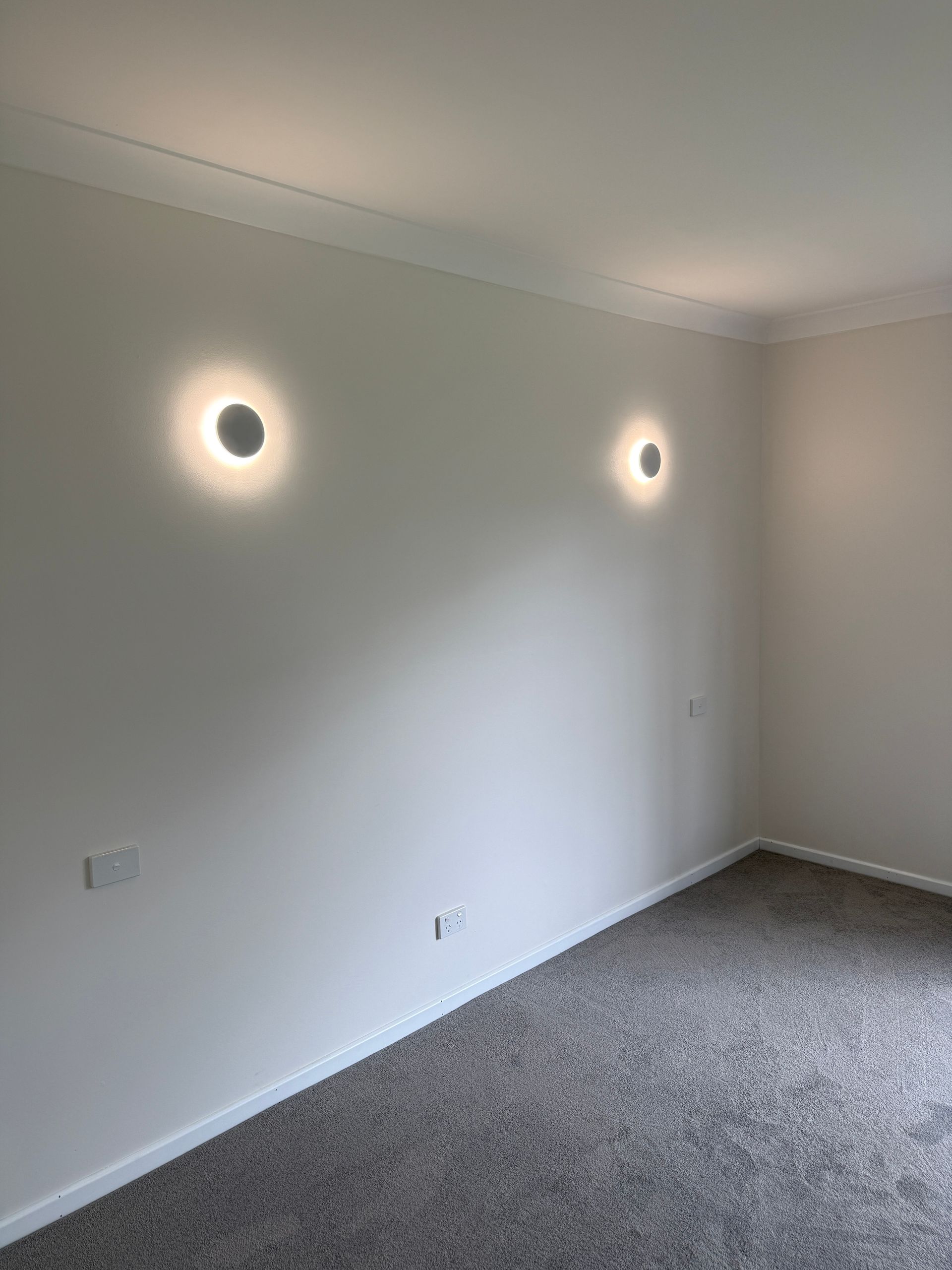 Empty room with gray carpet, white walls, and two wall sconces illuminating the wall — SparkSafe Electrical in Dapto, NSW