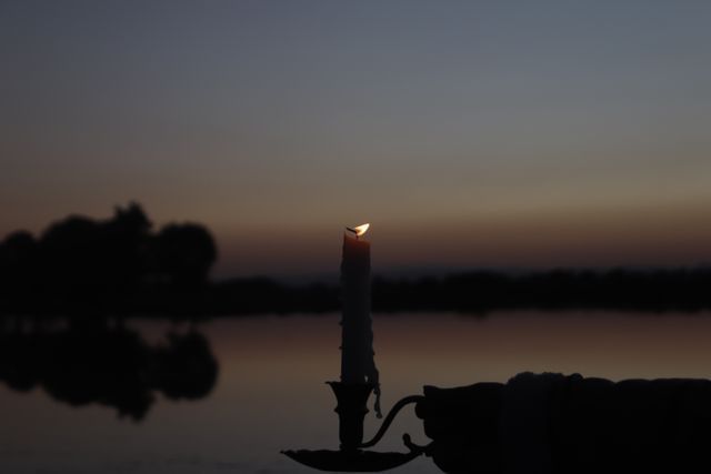 Silhouetted hand holding a candle during a peaceful lake sunset in Scarborough, ME, symbolizing remembrance and memorial services