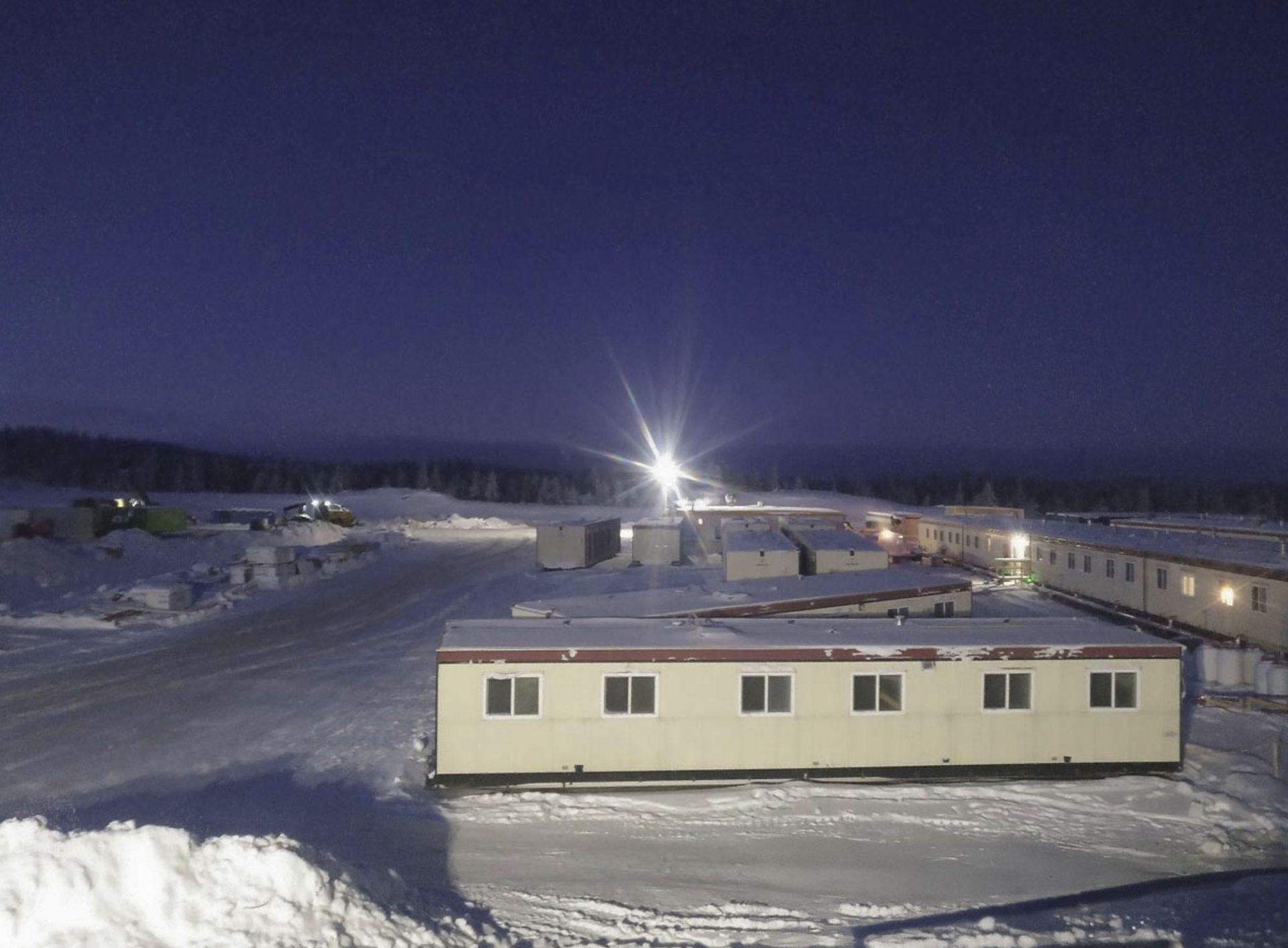 Snowy temporary accommodation and water treatment buildings at night under bright lights and a dark sky in Canada