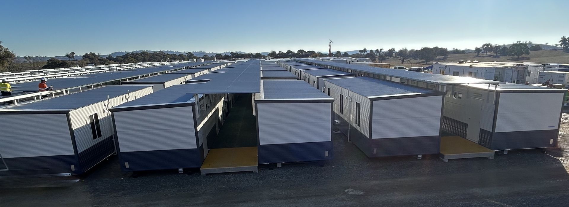 Rows of modular buildings, likely temporary housing, under a clear, blue sky.