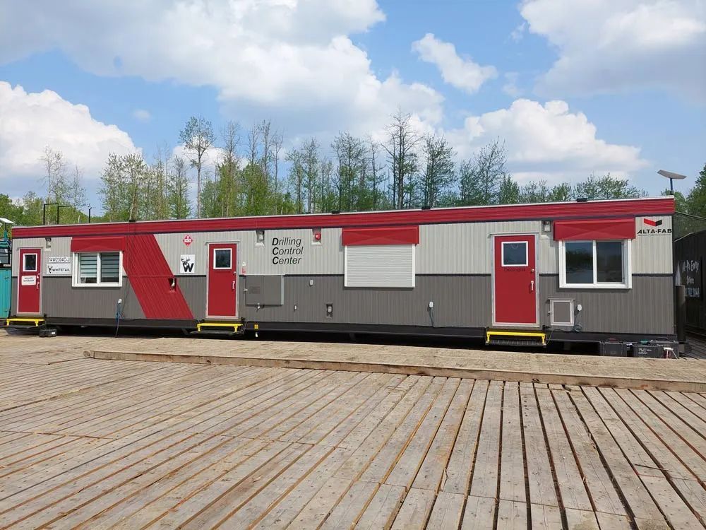 Mobile office building, red and grey with red doors, on a wooden platform.