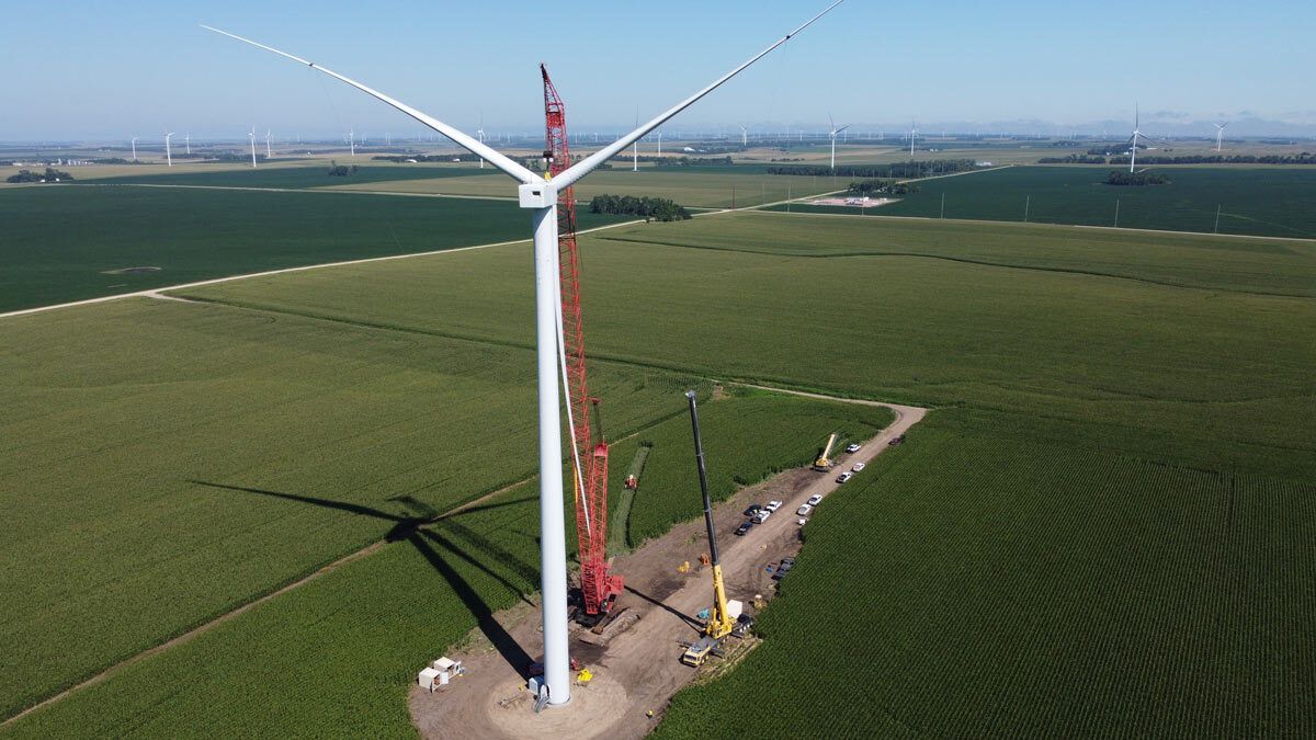 Wind turbine being maintained by a Centurion crane in a green farmland field, with a crane beside it.