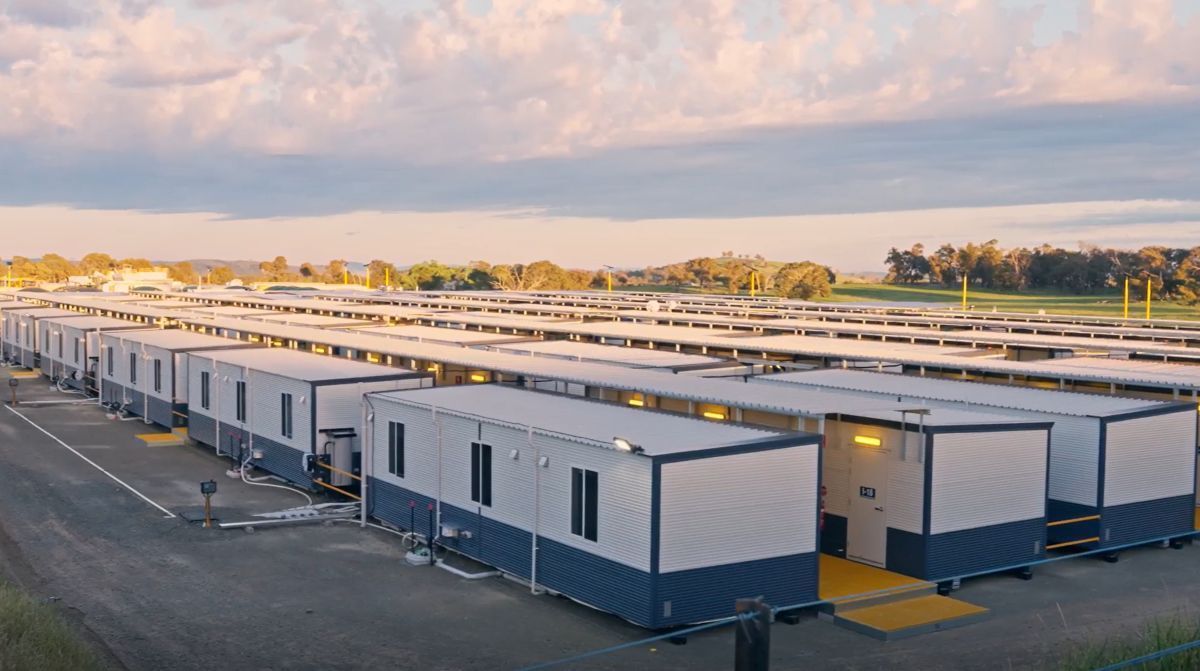 Large white modular buildings in a solar-panel-equipped industrial complex at sunset.