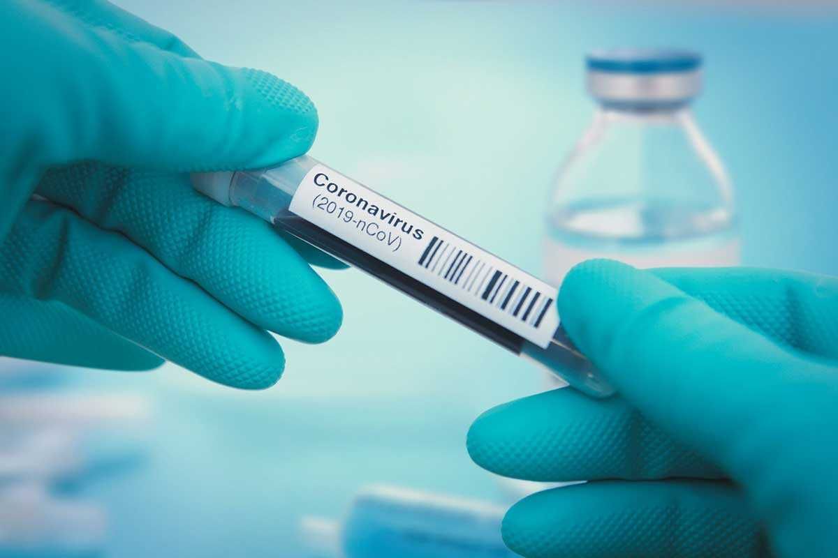 Gloved hands holding a labeled test tube in a lab setting supporting COVID 19 response