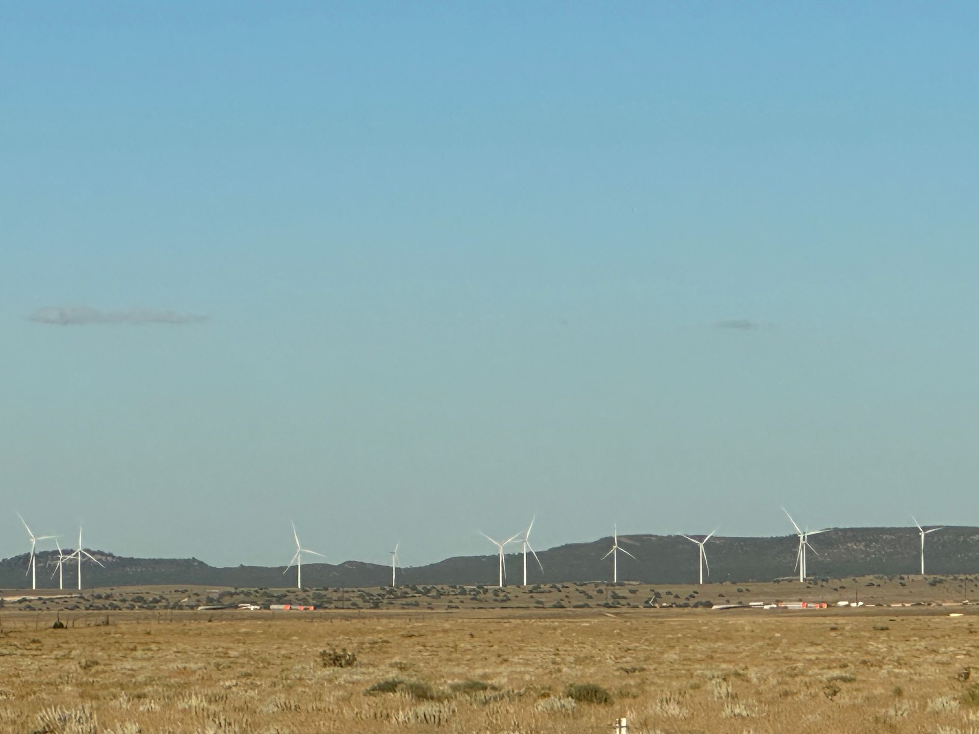 Wind turbines on a brown, grassy plain under a clear blue sky.