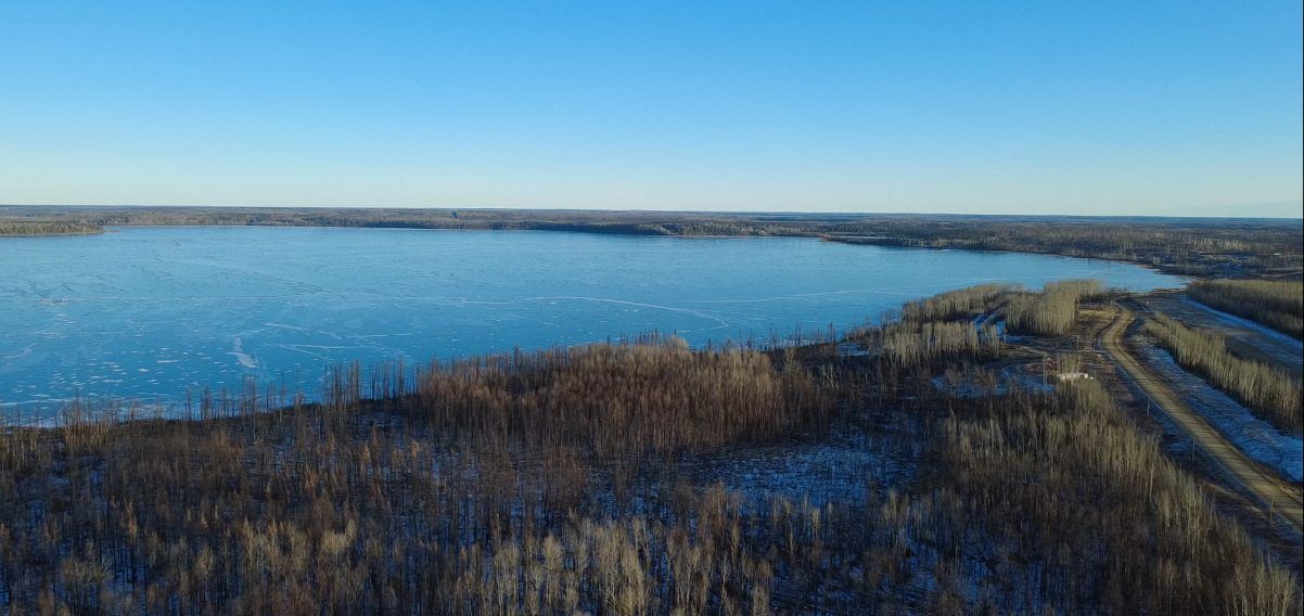 Aerial view of a frozen lake bordered by trees under a clear blue sky