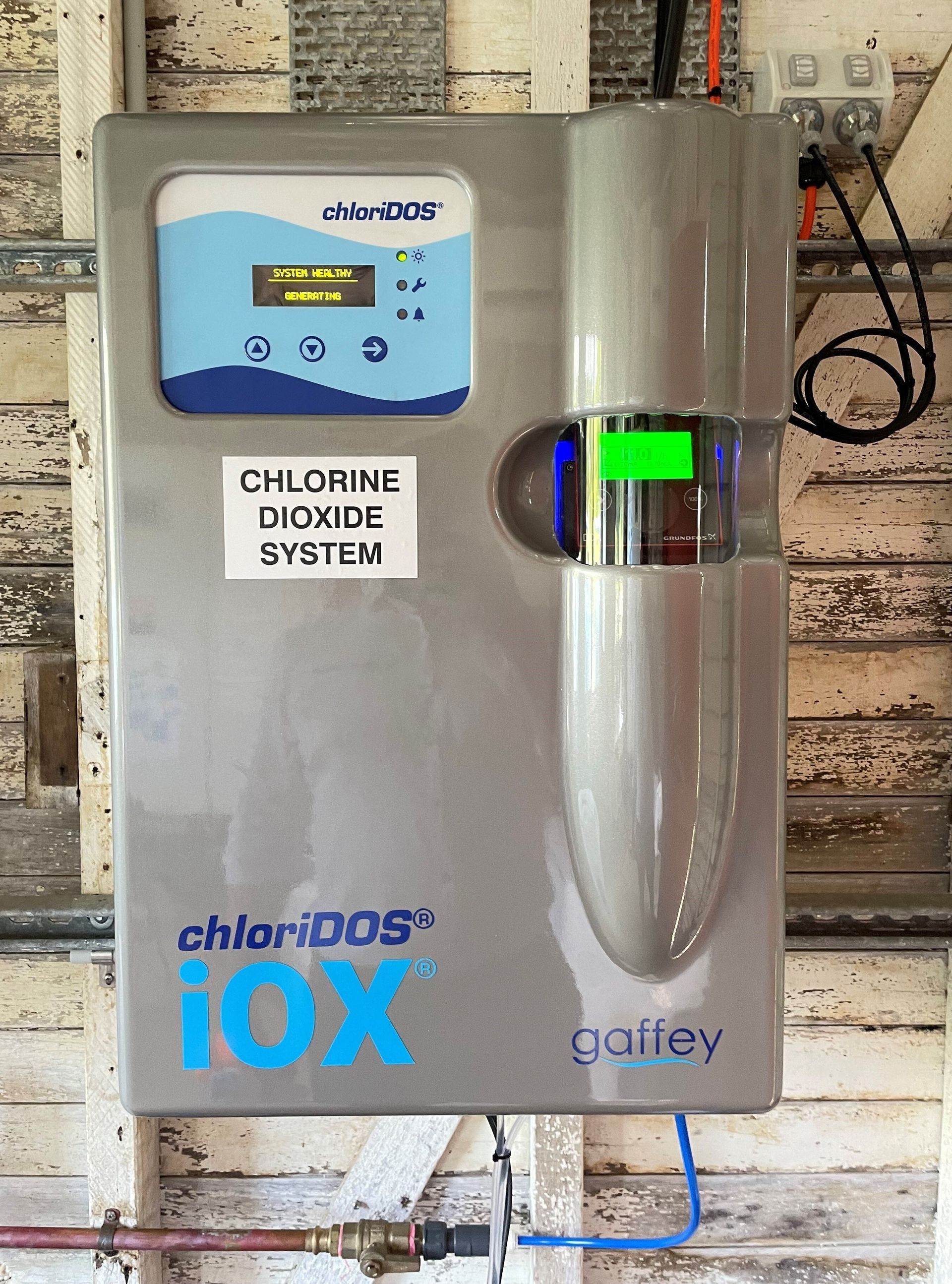 ChloriDOS iOX chlorine dioxide system on a wall; it has a digital display and clear cylinder.