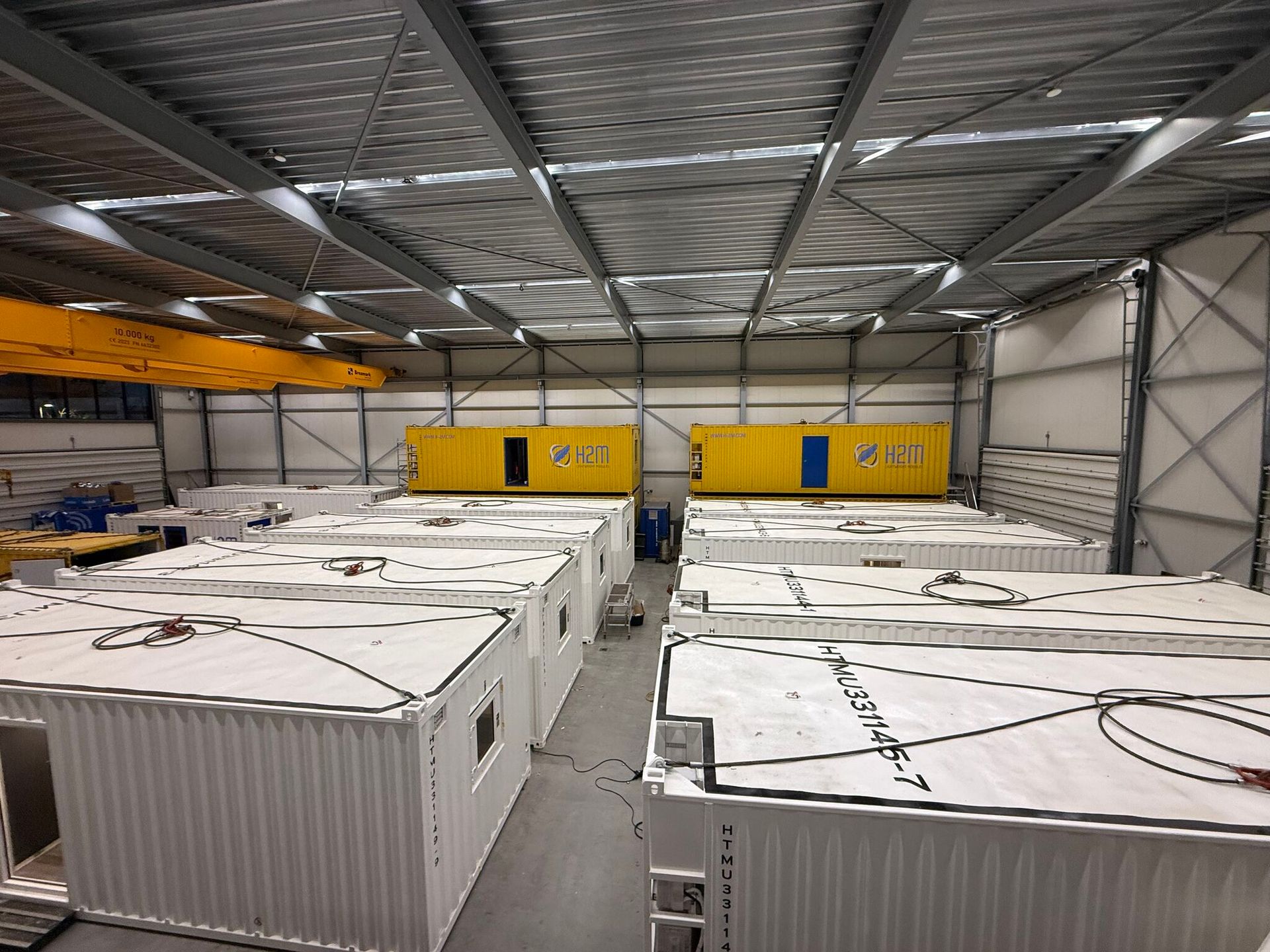 Warehouse interior with rows of large white shipping containers beneath a metal roof