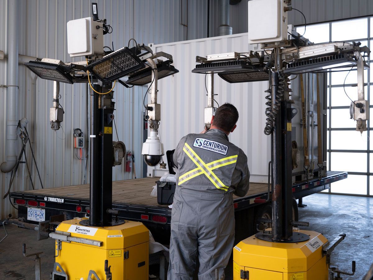 Man in gray jumpsuit adjusts security equipment mounted on two yellow mobile platforms.