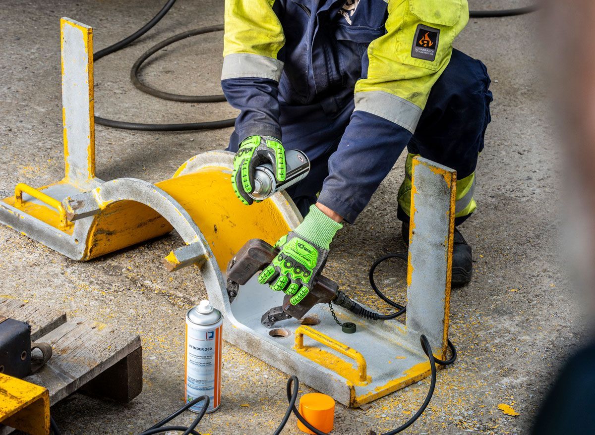 Person in workwear spraying a metal object, wearing gloves, in a workshop.
