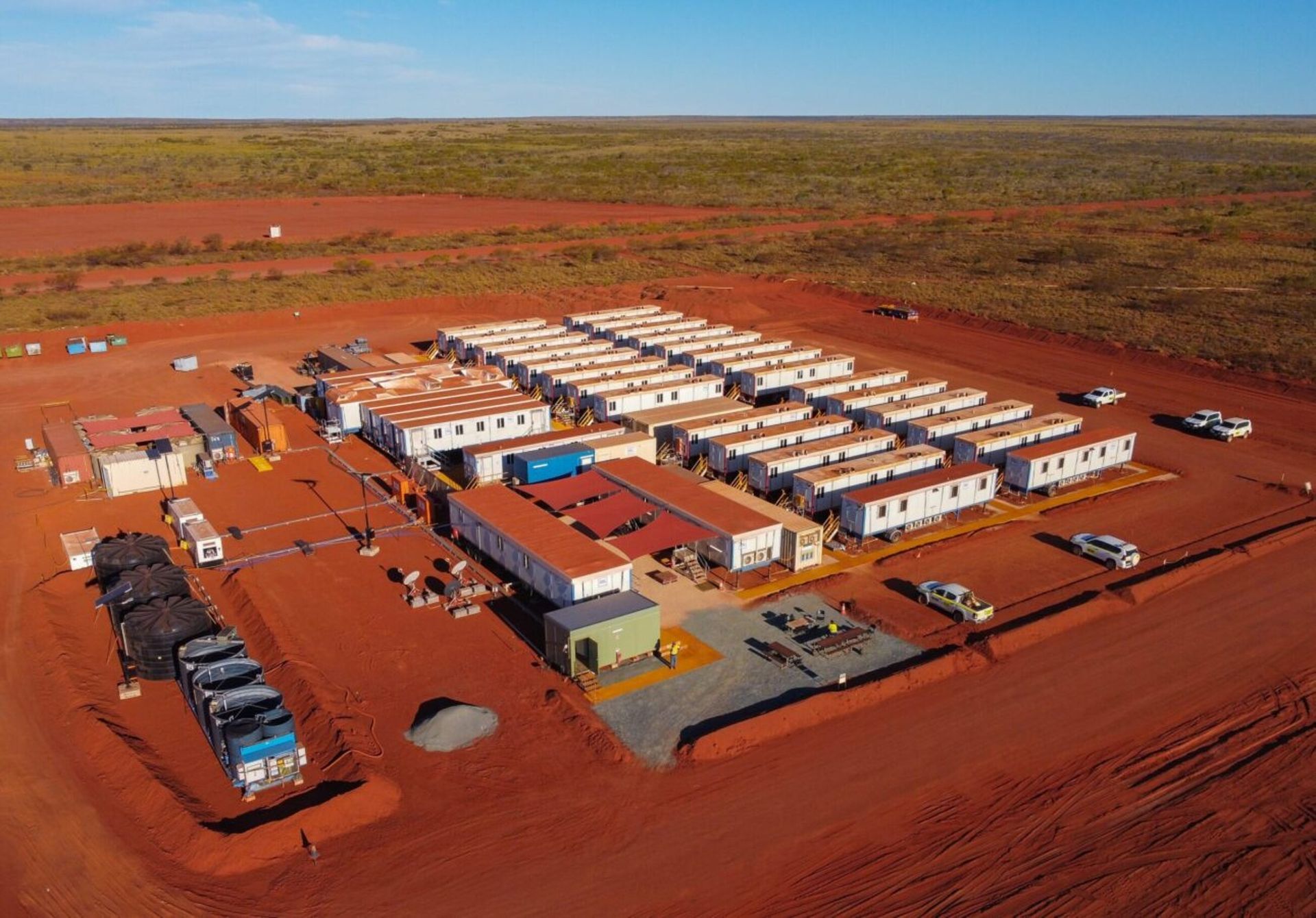 A cluster of white modular buildings with support vehicles on a flat, arid landscape under a blue sky.