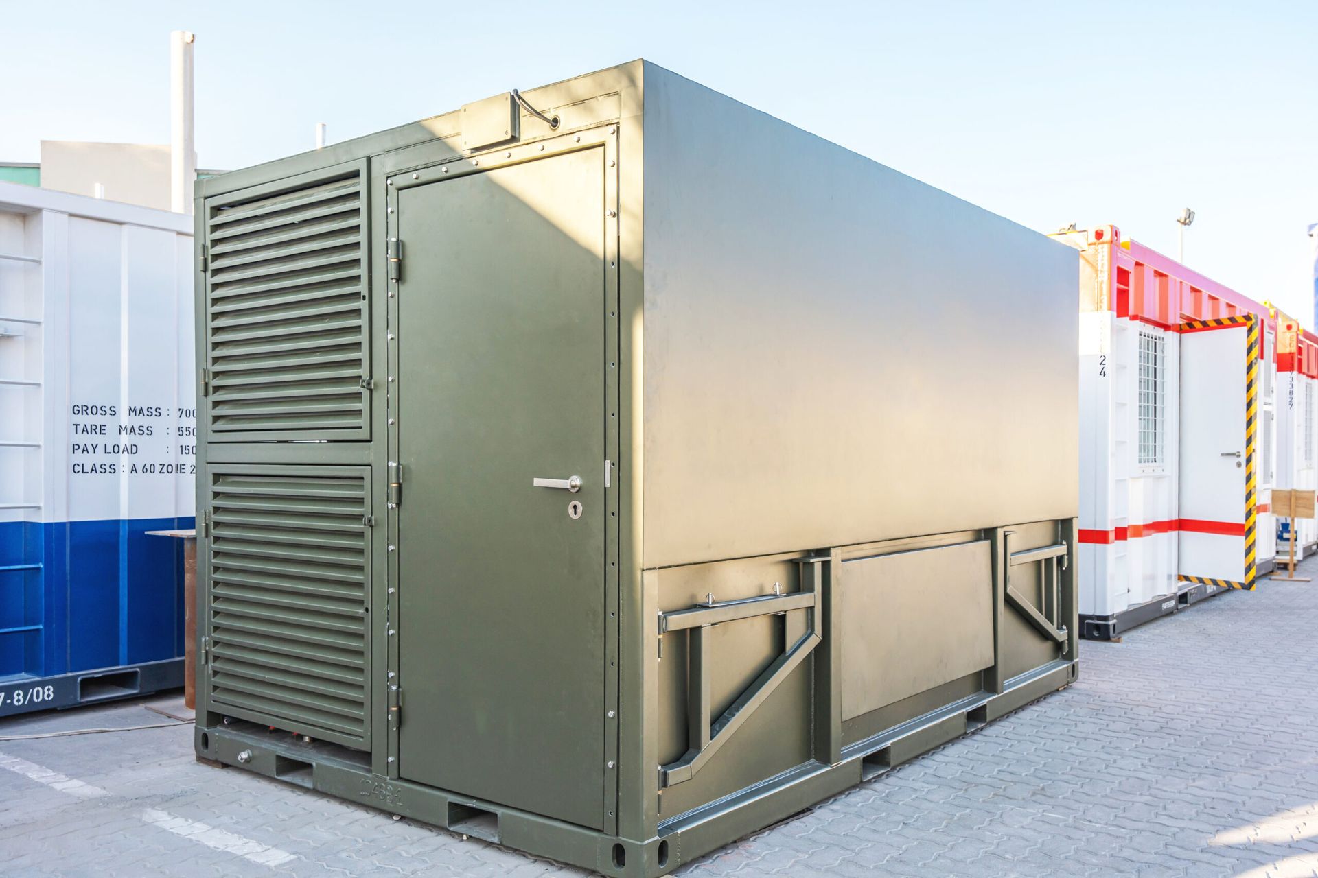 Olive-green industrial container with a door and side ventilation, parked outdoors.