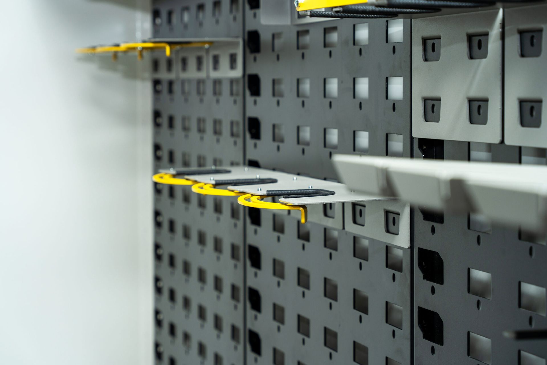 Close-up of a gray wall with several rows of slotted panels. Each row has a yellow shelf attached.
