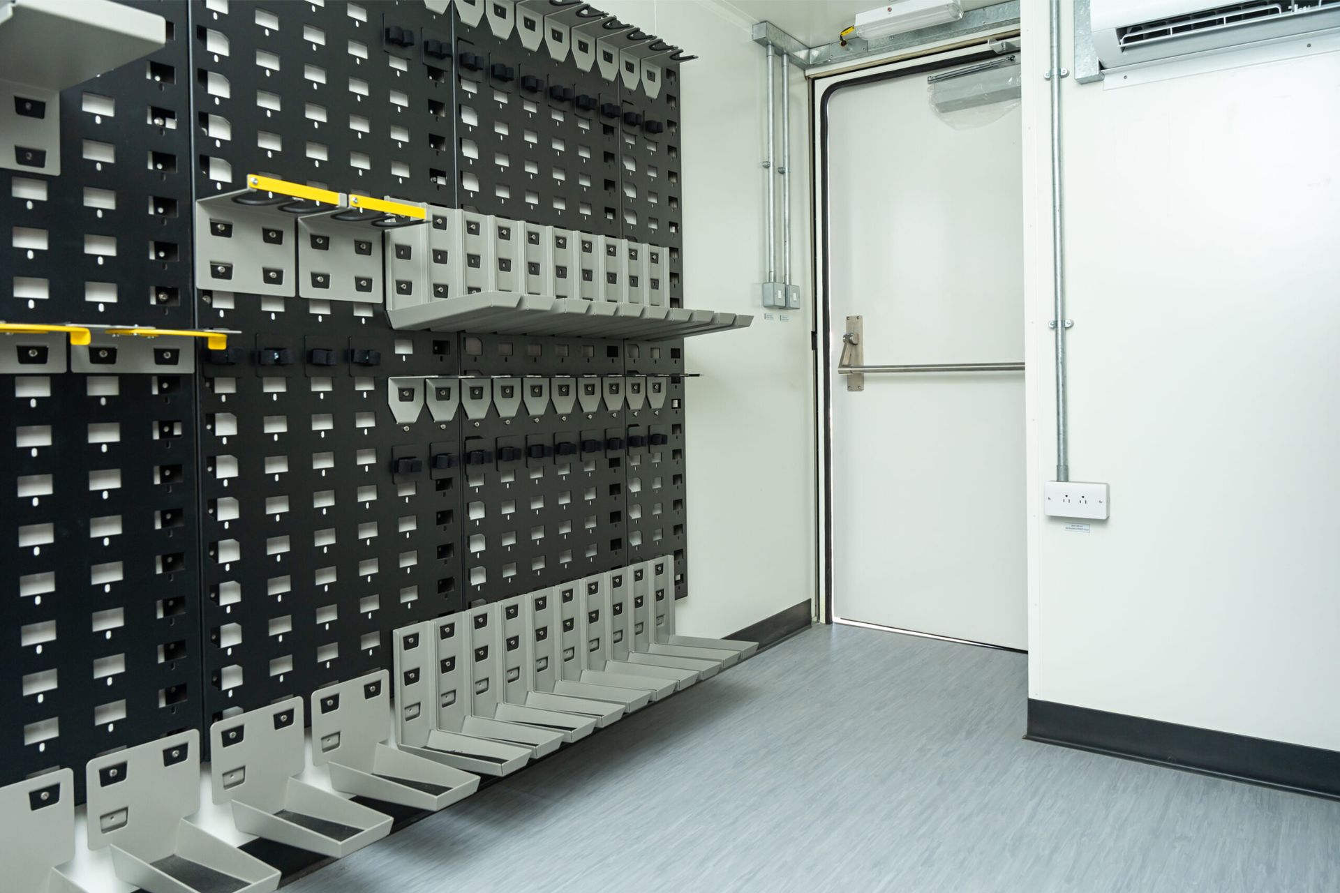 Black and gray storage racks line a room with a white door. Blue floor, white walls.