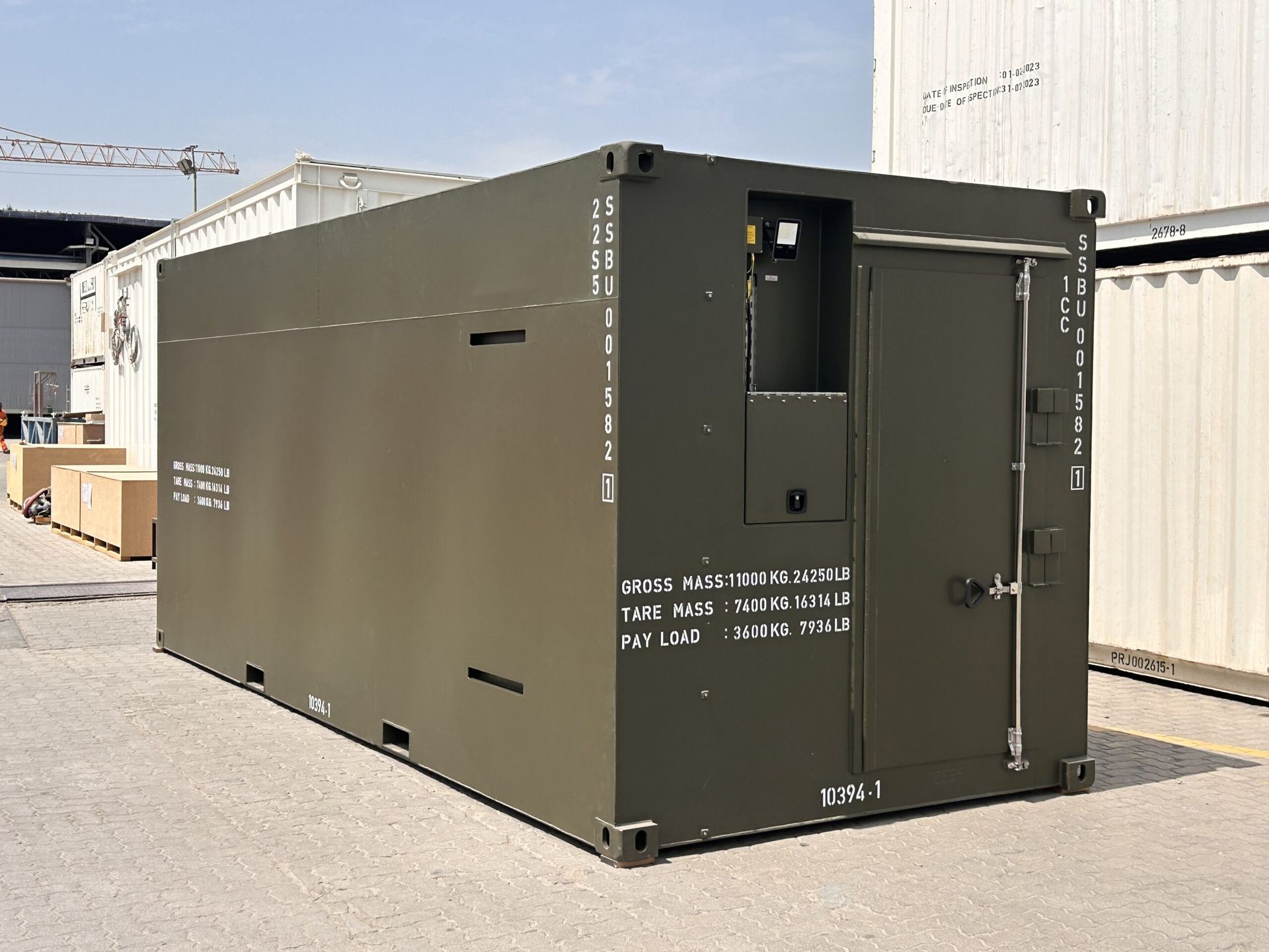 Olive green shipping container with a door and vents, sitting outside.
