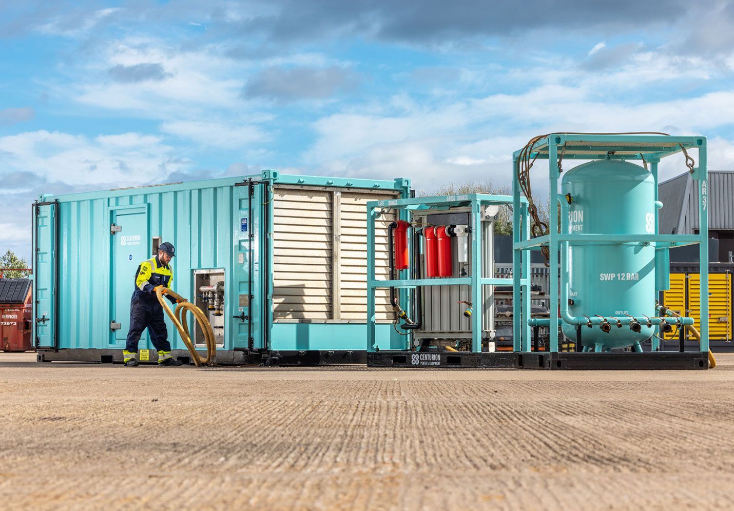A worker near turquoise industrial equipment outdoors.