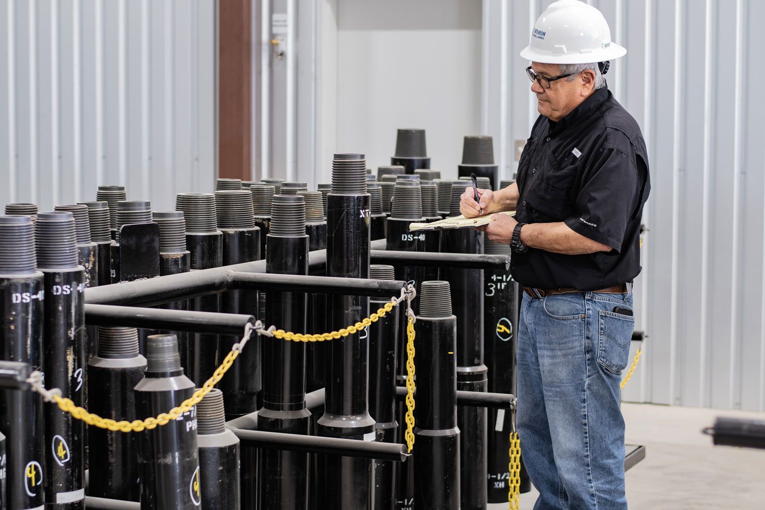 Man in hard hat inspects equipment in warehouse, taking notes.