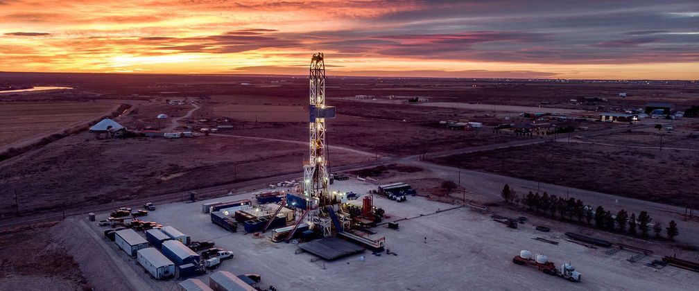 Oil drilling rig at sunset. Rural, open landscape with a vibrant sky.