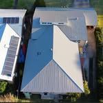 Overhead view of two houses with light gray metal roofs, one with solar panels.