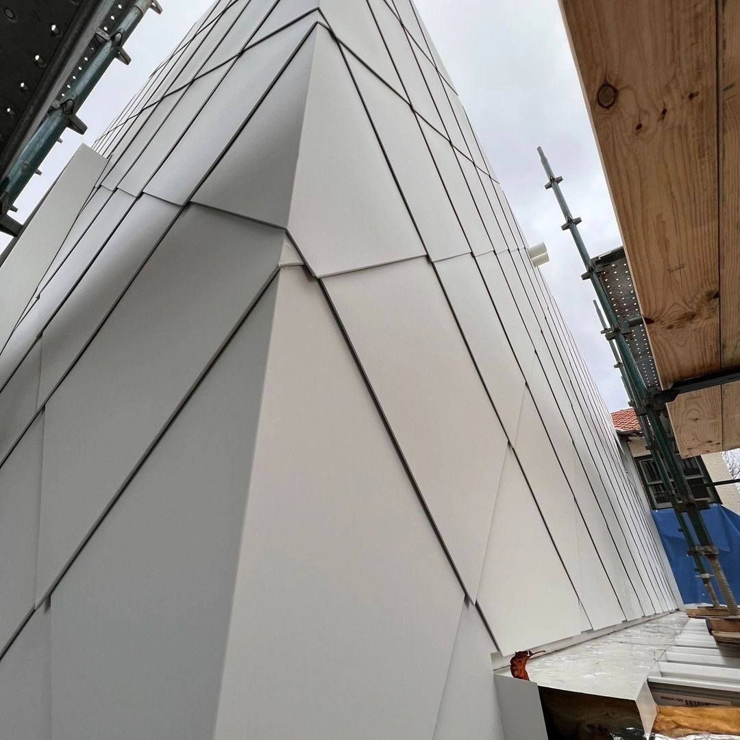 Exterior of building with light gray geometric panels, scaffolding visible.