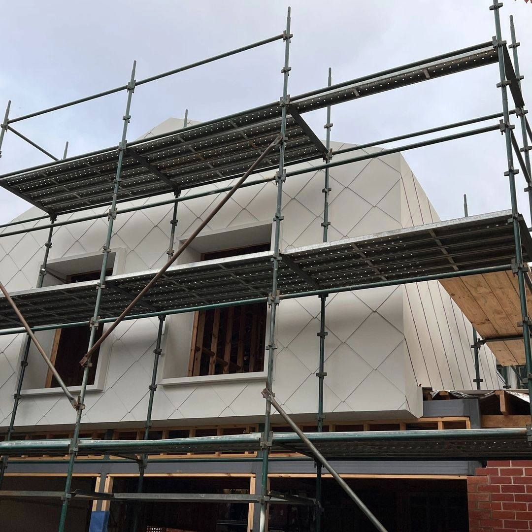 Scaffolding surrounds a house under construction with white walls and two windows.