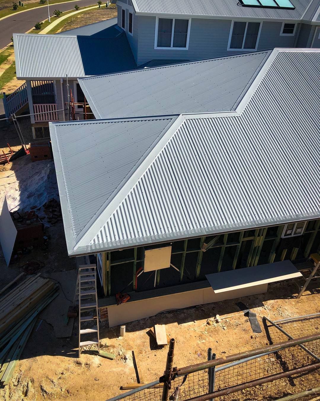 Construction site with a partially built house; gray corrugated metal roof and wooden frame are visible.