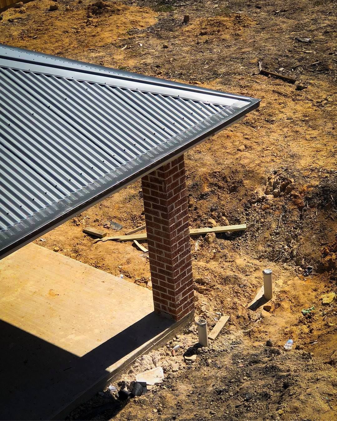 Brick pillar supporting a corrugated metal roof on a building under construction.