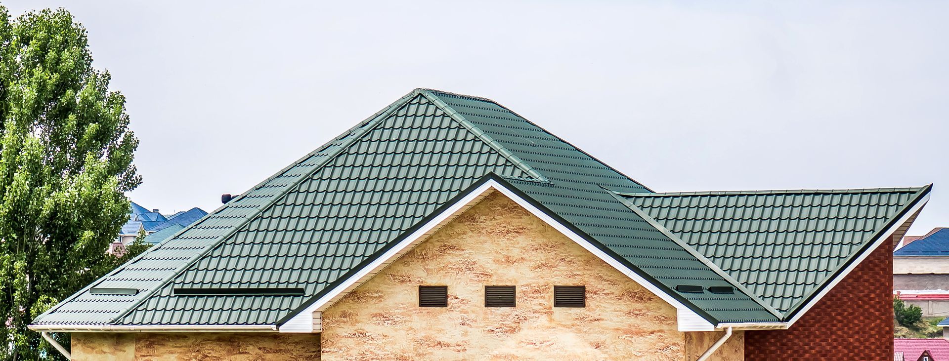 Brick house with green tiled roof and dormer windows under a clear sky