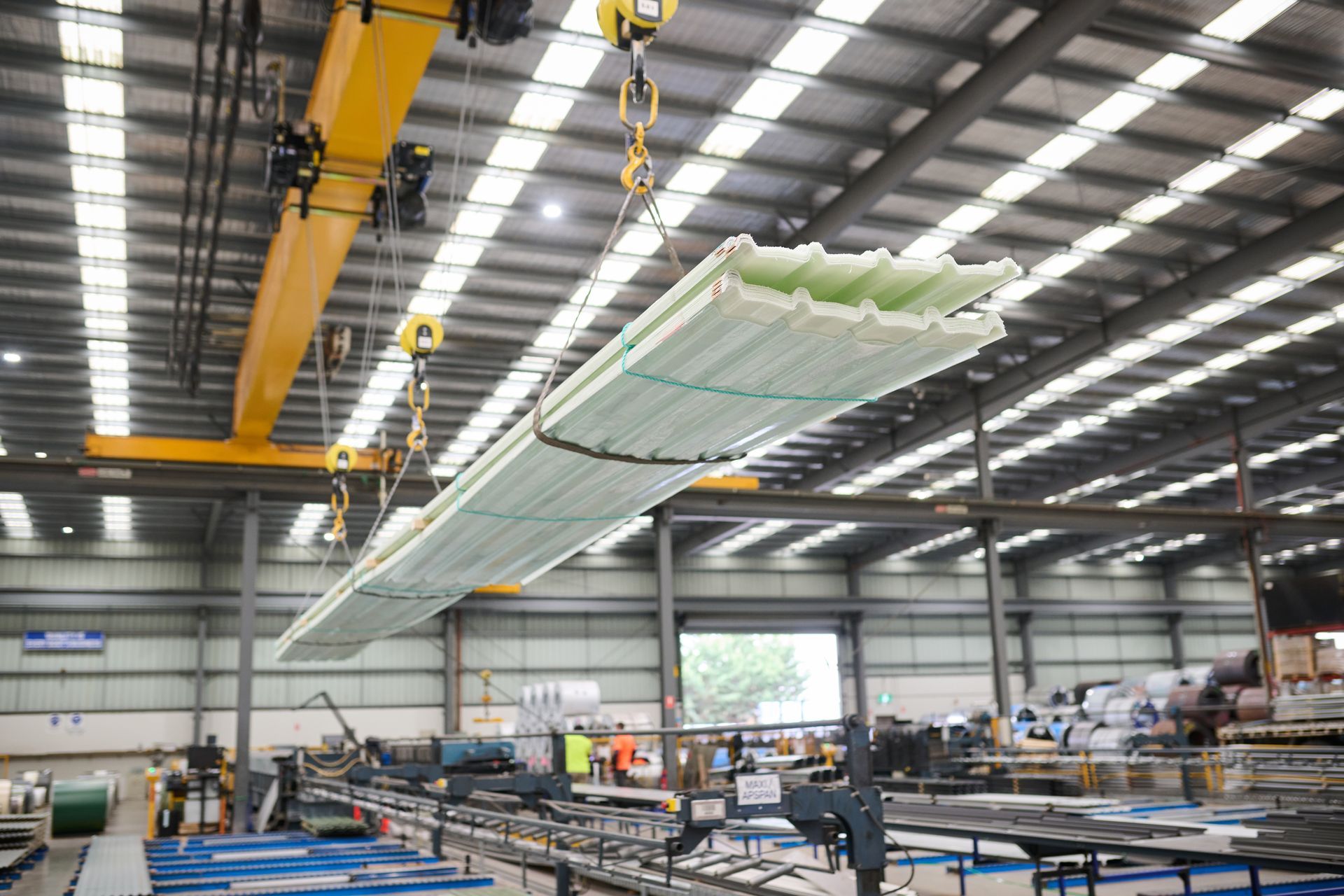Crane lifting a bundle of long, rectangular fiberglass panels in a factory.