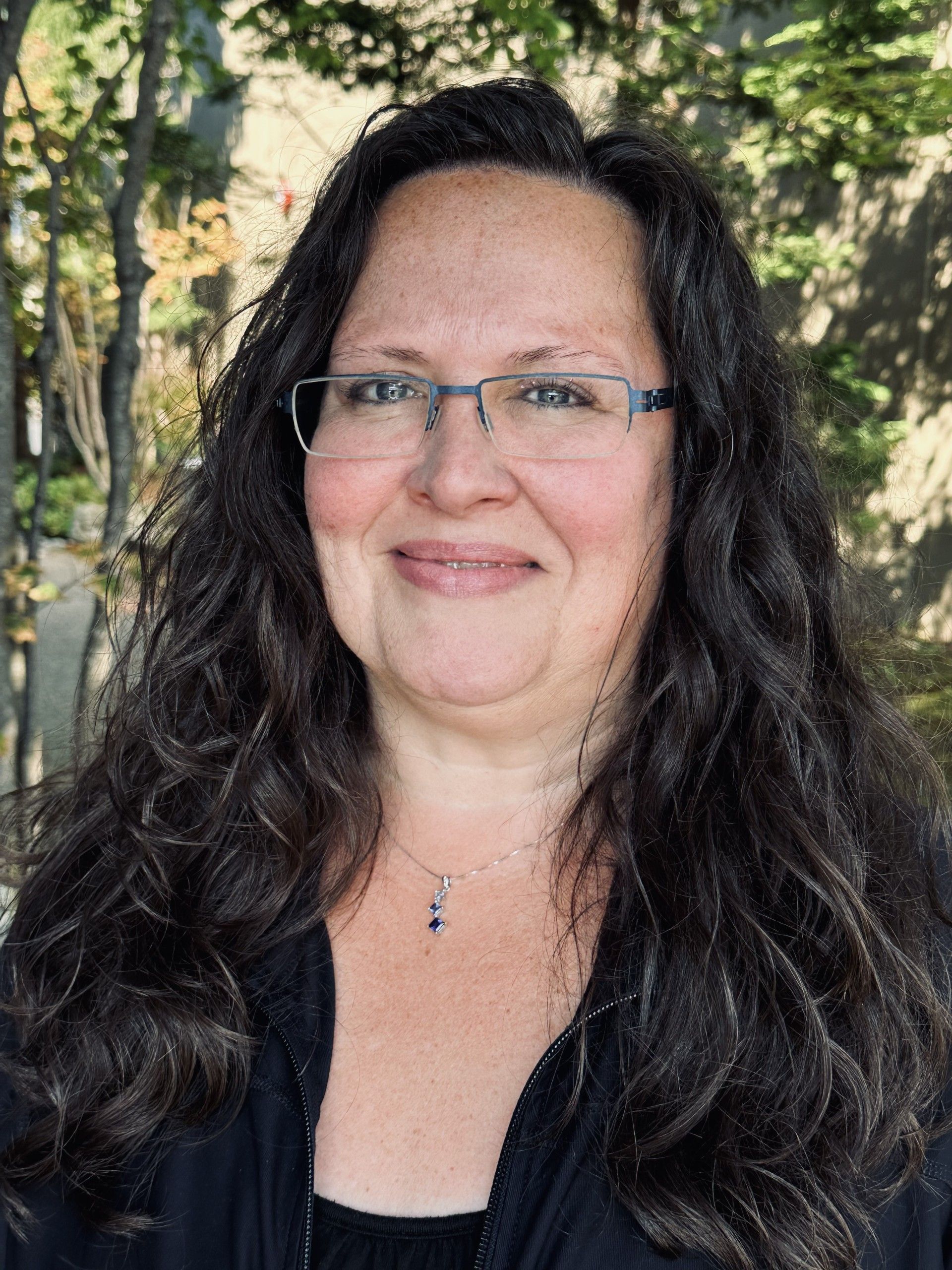 A woman wearing glasses and a black shirt is smiling for the camera.