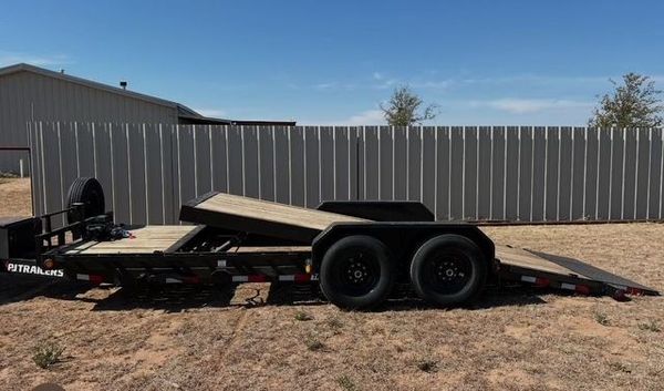 A trailer is parked in the dirt in front of a fence.