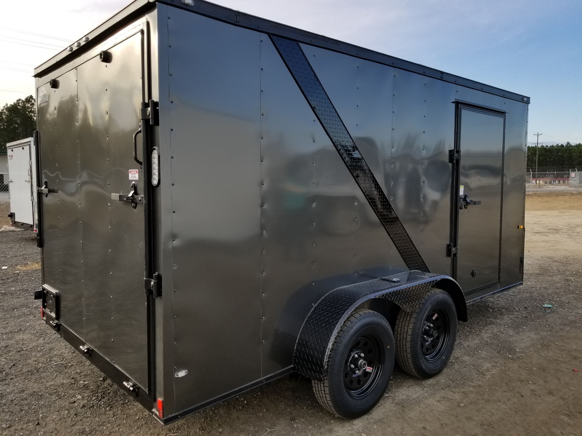 A black trailer is parked in a dirt lot.