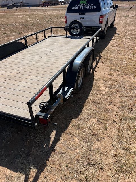A white truck is towing a trailer on a dirt road.