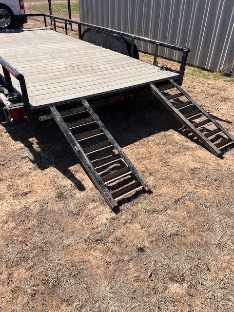 A trailer with ramps attached to it is parked in the dirt.