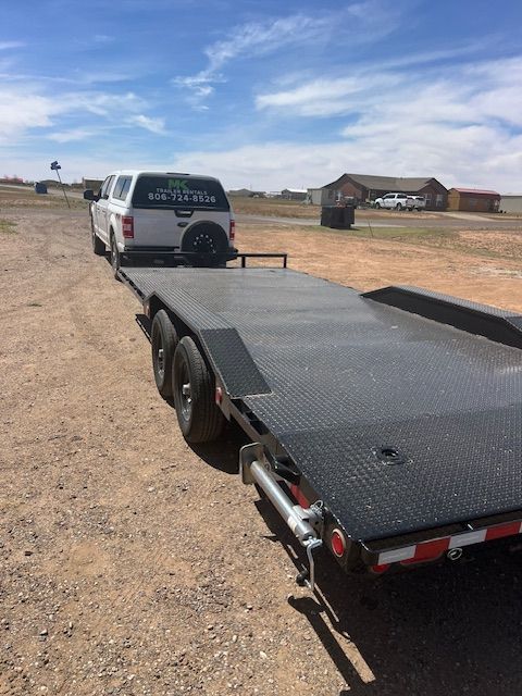 A truck is towing a trailer in a dirt field.