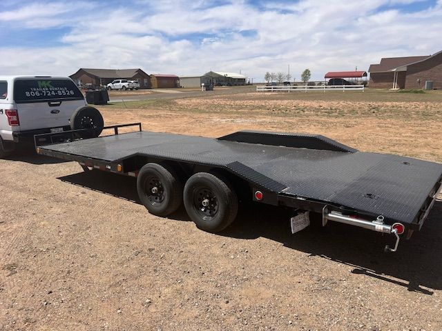 A white truck is towing a flatbed trailer in a dirt field.