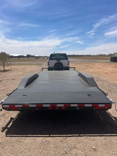 A truck is sitting on top of a trailer in a dirt field.