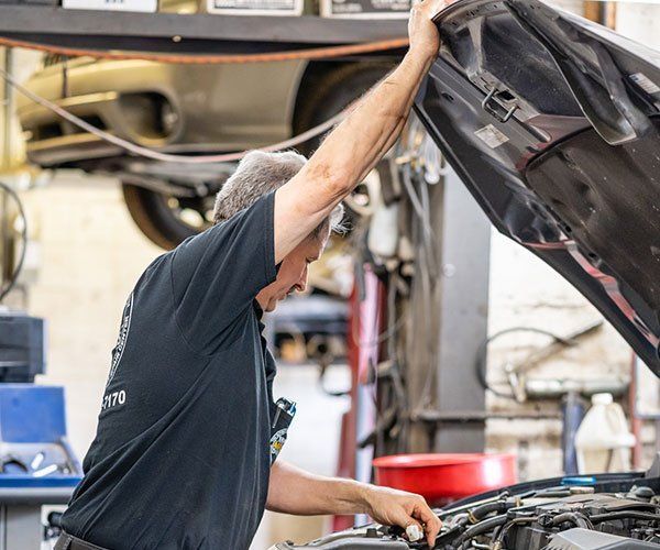 A man is working on a car with the hood up in a garage.