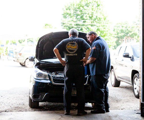 Two men are looking under the hood of a car in a garage.