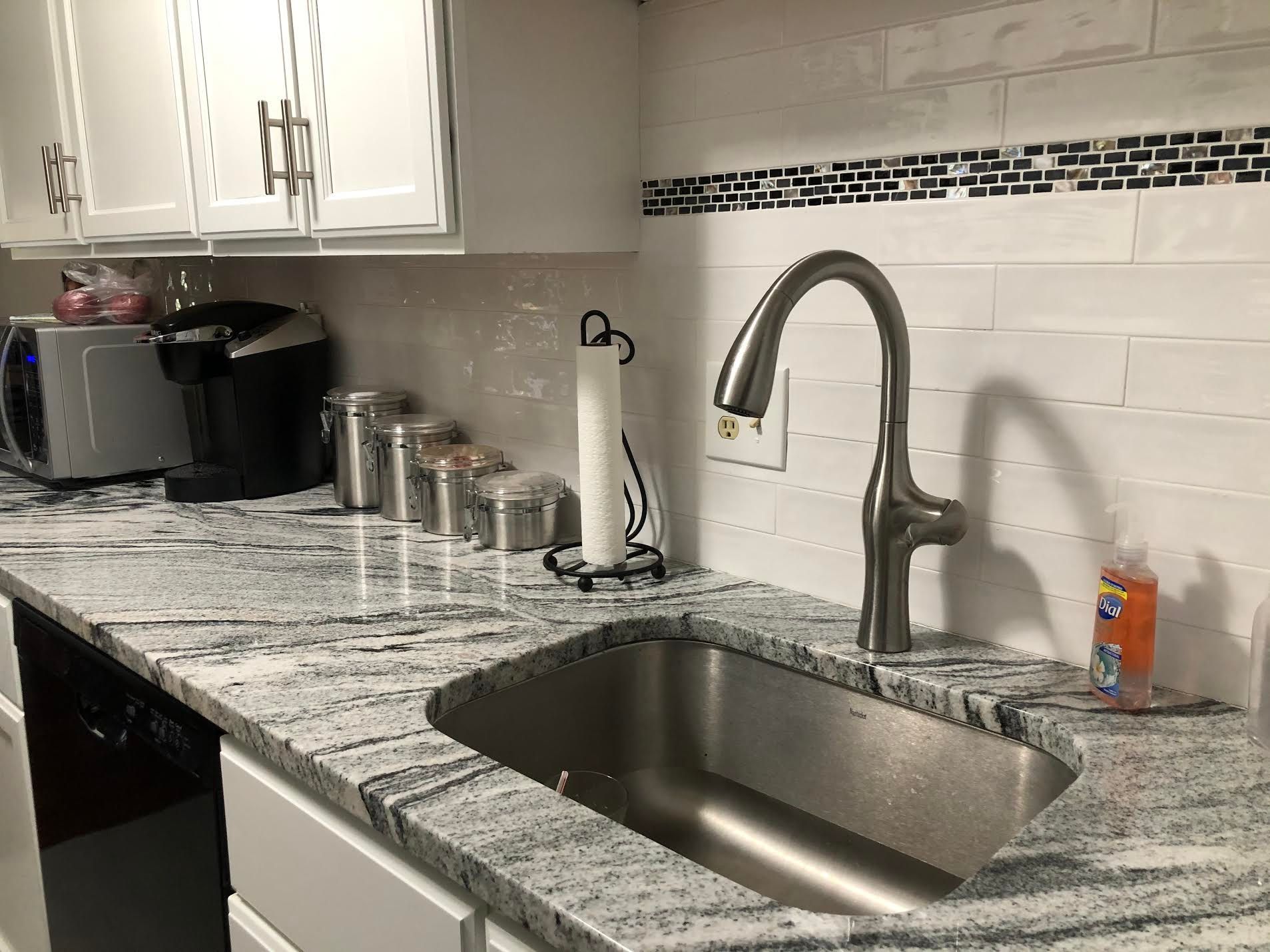 A kitchen with granite counter tops and a stainless steel sink.