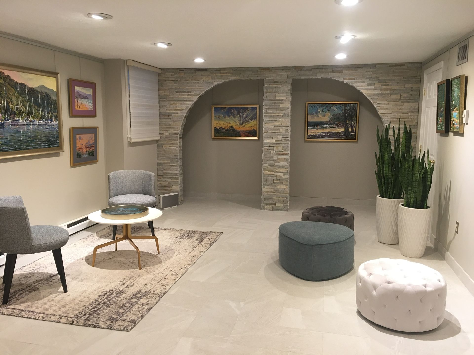 A living room with a table , chairs , ottomans and paintings on the wall.
