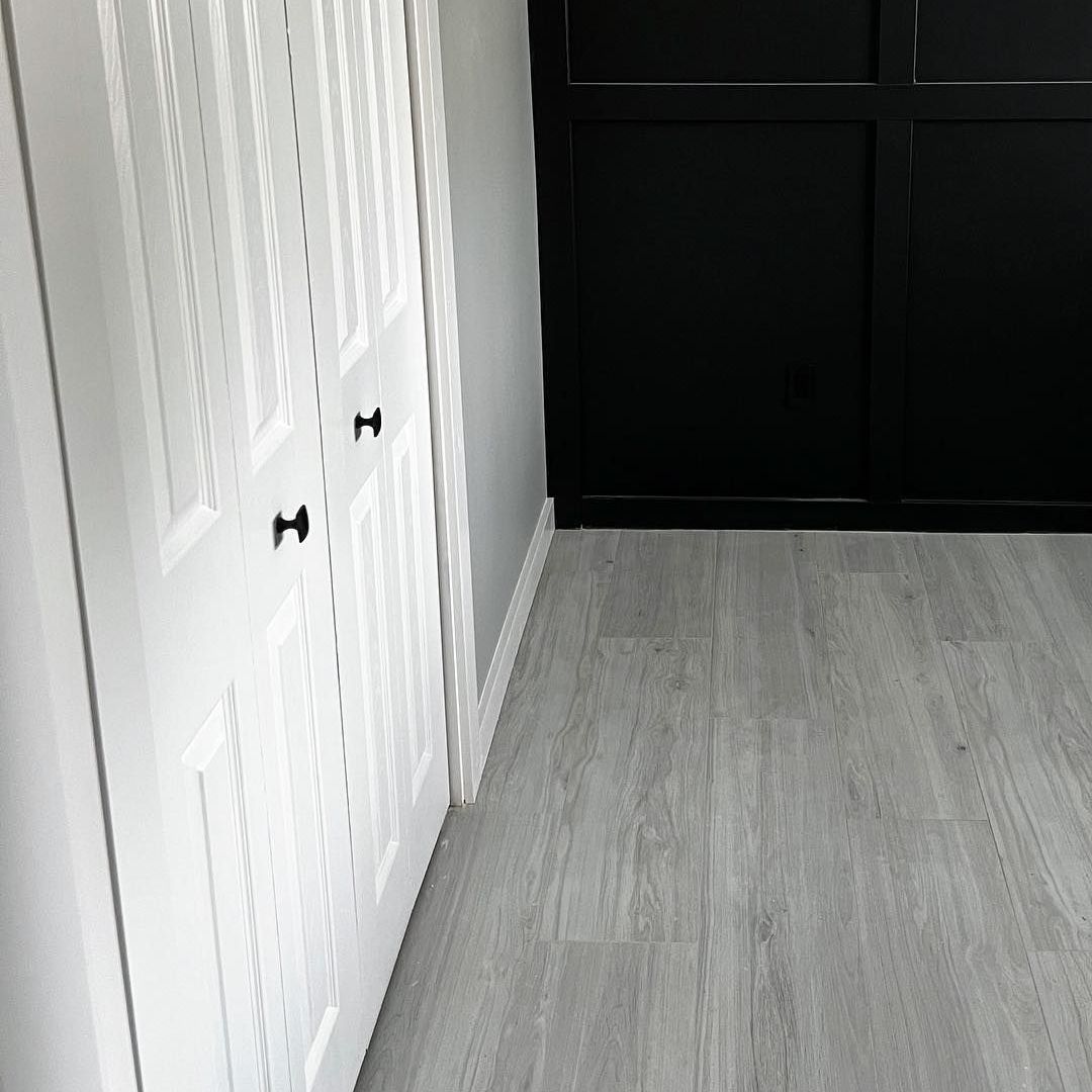A hallway with white cabinets and black doors and a wooden floor.