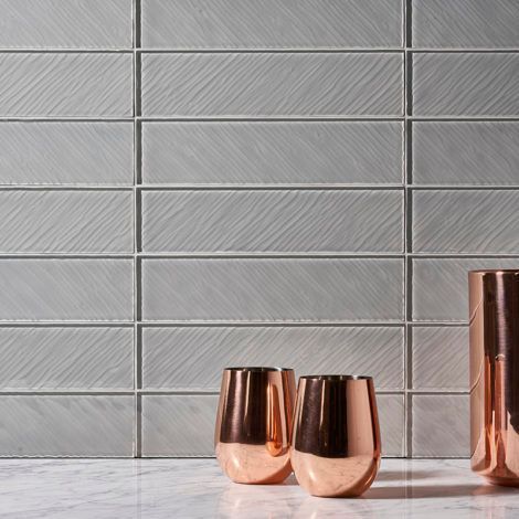 Three copper cups are sitting on a counter in front of a tiled wall.
