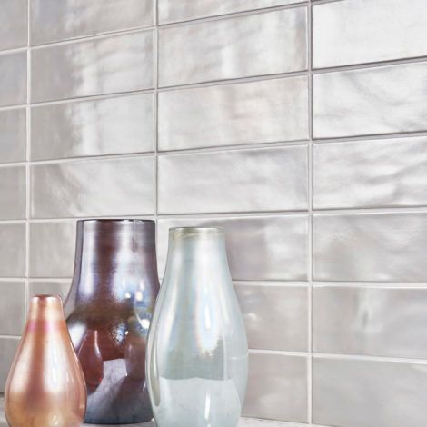 Three vases are sitting on a counter in front of a tiled wall.